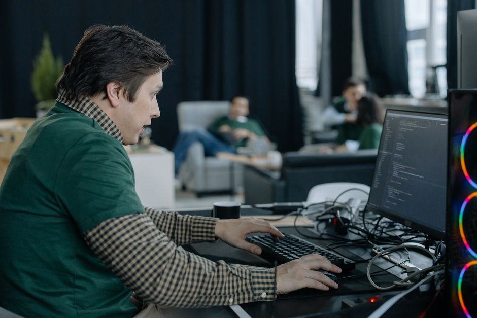 Programer koncentriran na kodiranje na računalu u suvremenom uredskom okruženju.